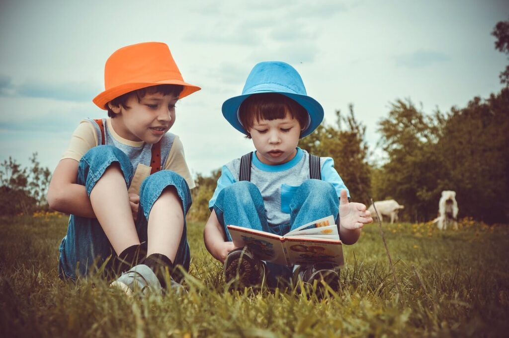 オレンジと水色のハットを被った男の子たちが本を一緒に読んでいる