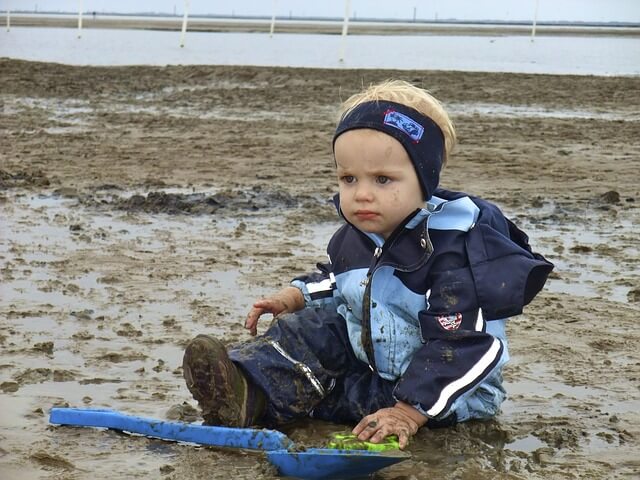 幼児の男の子が泥の中で呆然とスコップの前に座っている