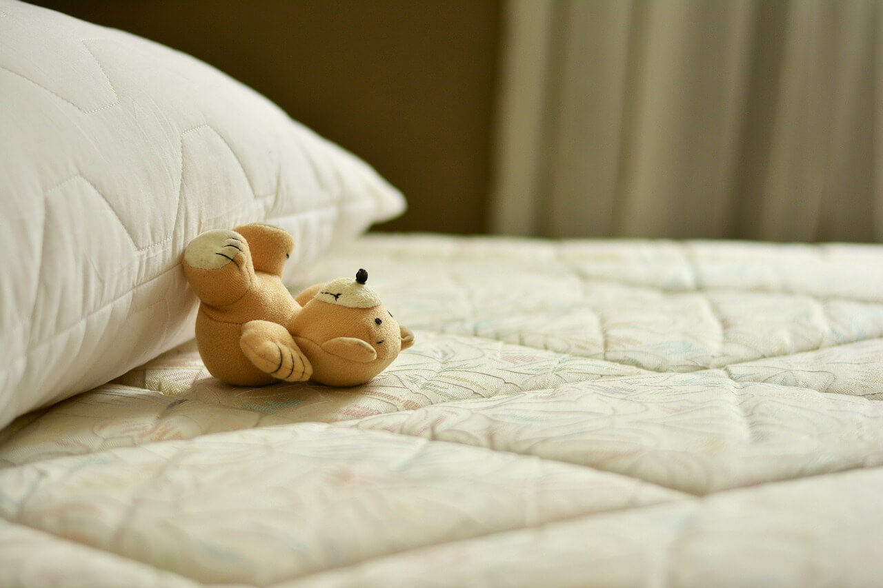 ベッドマットレスの上にクマの人形と枕がある